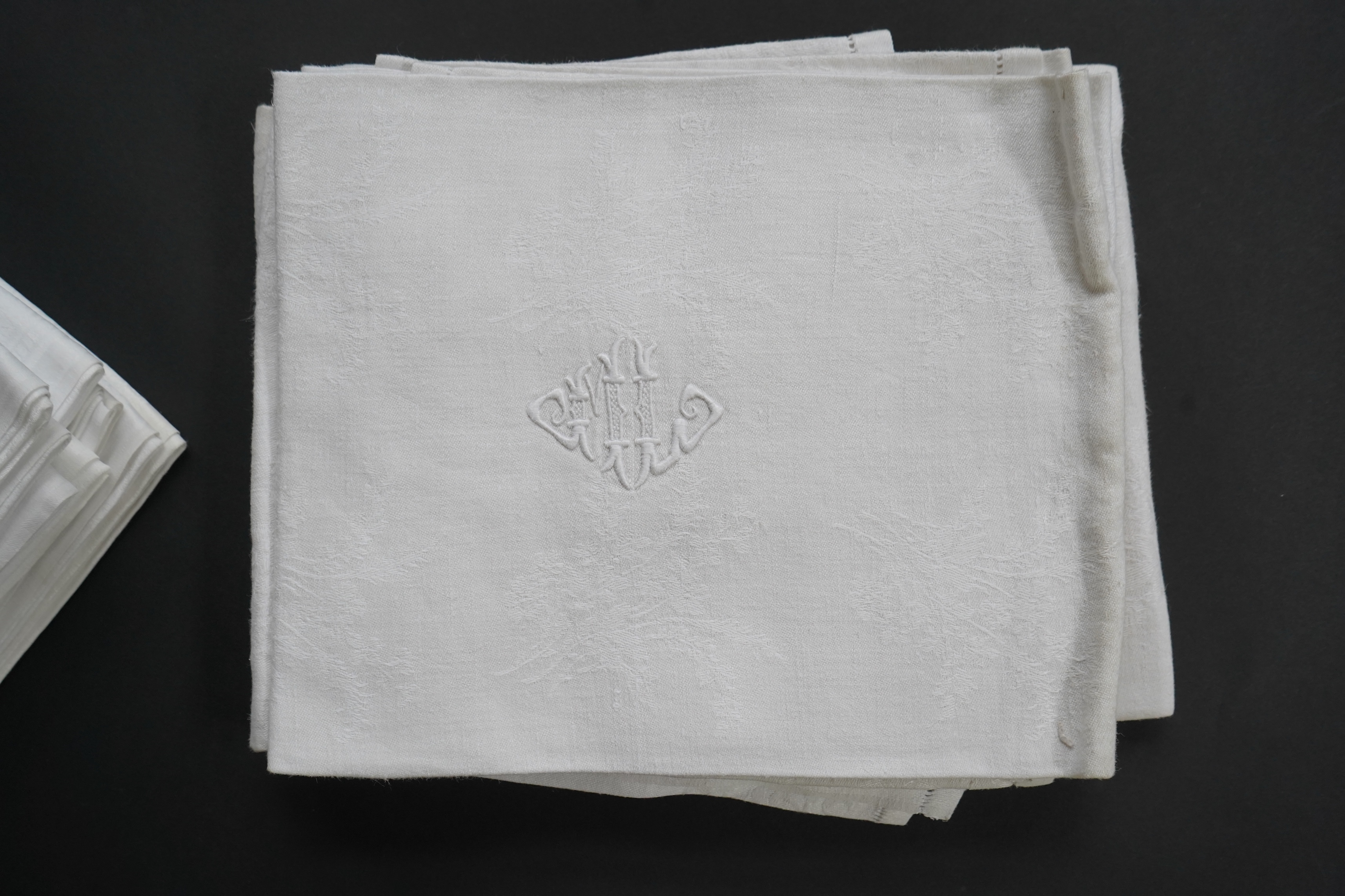 A set of nine red monogrammed 19th century large damask dinner napkins and a similar set of coarser French provincial damask napkins, the large set, decoratively designed with a boating river scene, amongst classical bui